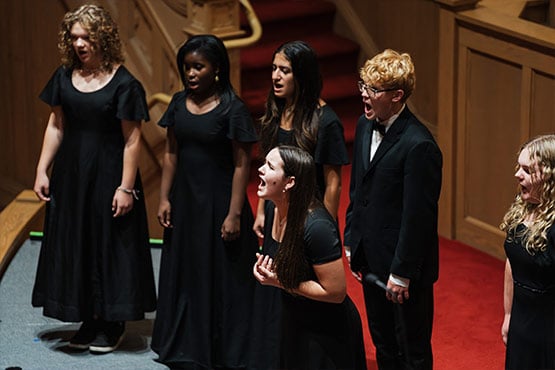 A group of singers in black dresses and a tuxedo performing on stage.