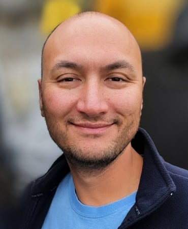 Jonathan Alexander "Jonny" Quinton wearing a blue shirt and a dark jacket, standing outdoors with a blurred background.