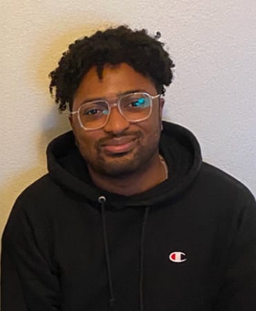 Kozon G. Thomas wearing a black Champion hoodie against a plain light-colored wall.