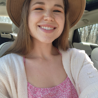 Chloe Summers smiling inside a car, wearing a wide-brimmed hat, a pink floral top, and a white cardigan.