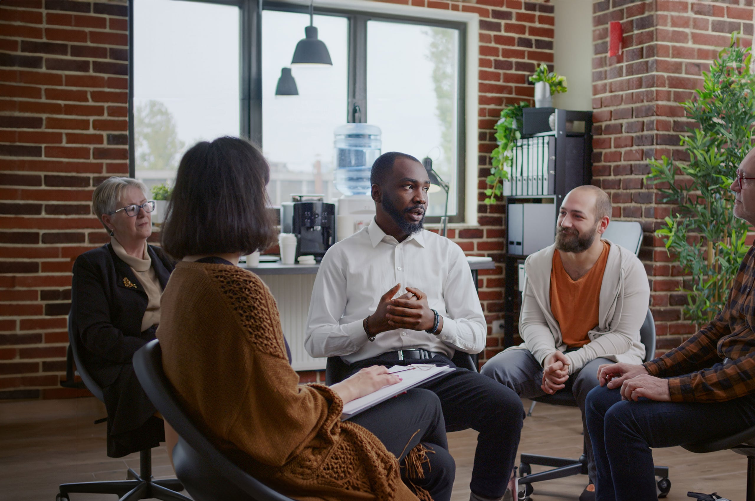 A group of people sitting in a circle in a modern office setting, engaged in a discussion.