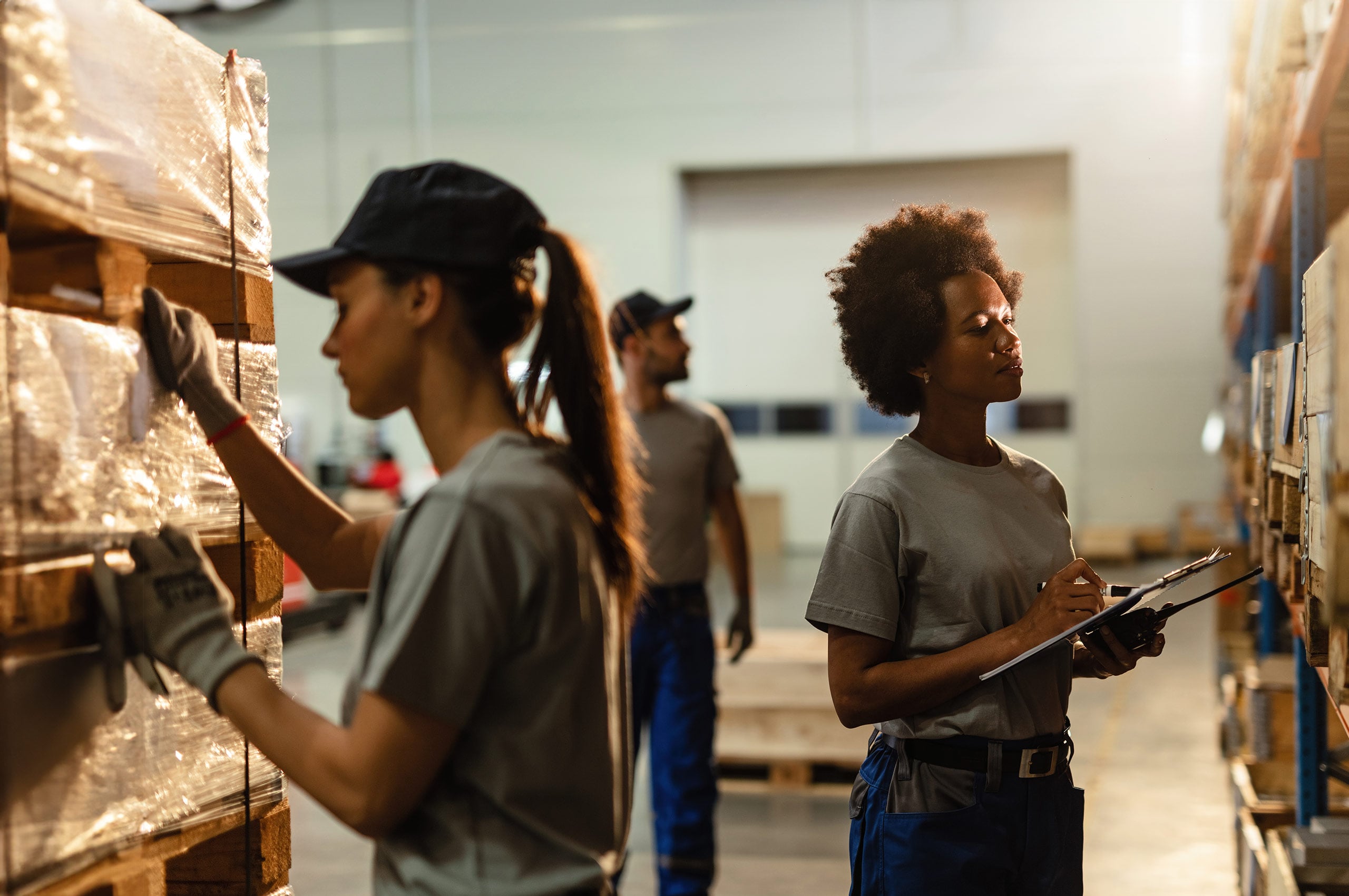 Warehouse workers organizing and checking inventory on pallets, with one person holding a clipboard.