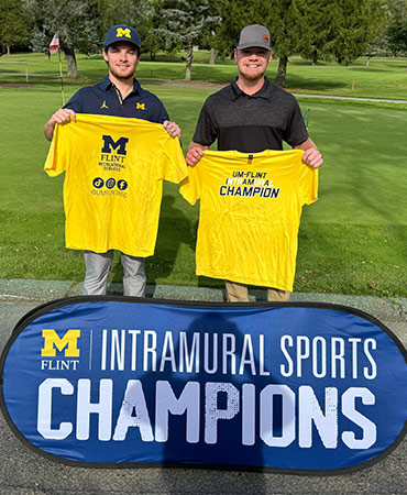 Two individuals hold yellow t-shirts celebrating their victory in intramural sports, with a banner reading 