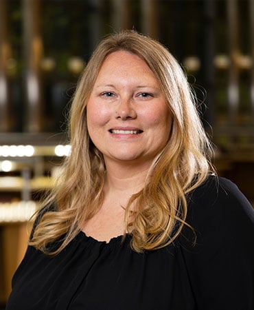 Tameka Shepard smiles for a professional headshot. She is wearing a long-sleeved, black blouse. Her long strawberry-blonde hair is hanging down onto her shoulders and chest.