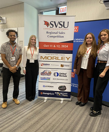 Four people standing beside a banner for the SVSU Regional Sales Competition on October 11 and 12, 2024, with sponsor logos including Morley, United Rentals, and others.