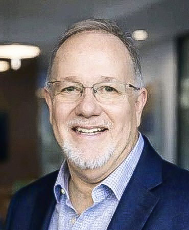 John Waldo smiles for a portrait. He is wearing a blue blazer, light-blue shirt and glasses. He has grayish-brown hair and a white goatee.