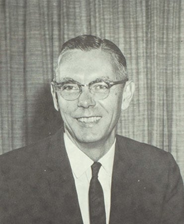 A black and white portrait of David French wearing a suit and tie, with a textured background.