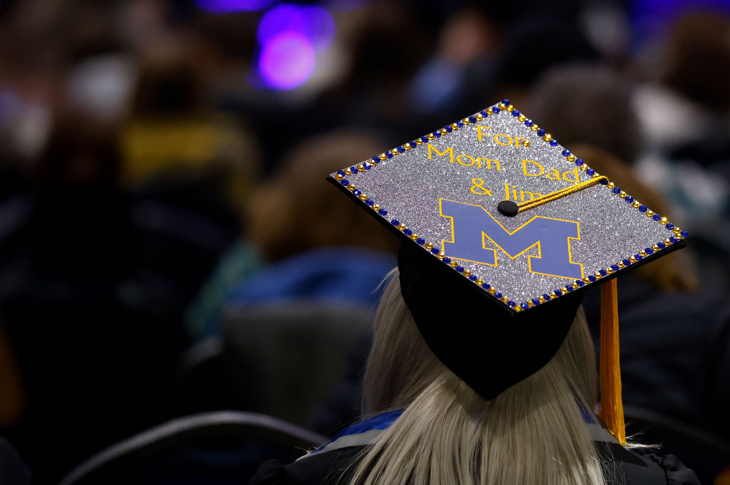 A graduate wears a glittery cap decorated with a University of Michigan logo and a message that reads, “For Mom Dad & Jim.”