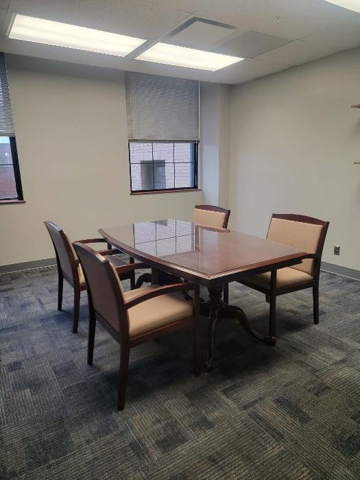 Conference room with a rectangular wooden table and four beige cushioned chairs on a blue carpeted floor.